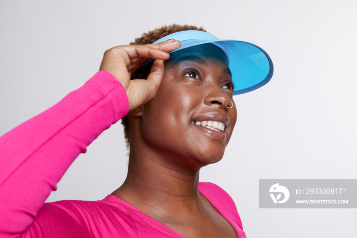 Studio portrait of smiling woman wearing blue sun visor and pink shirt