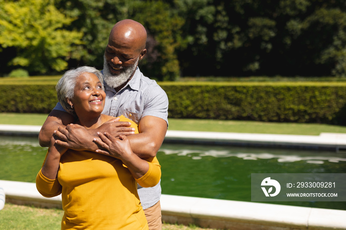 Senior african american couple spending time in sunny garden together embracing and smiling