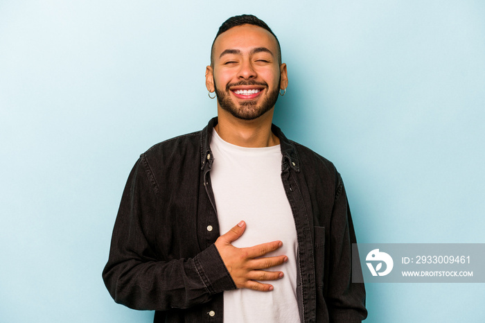 Young hispanic man isolated on blue background touches tummy, smiles gently, eating and satisfaction concept.