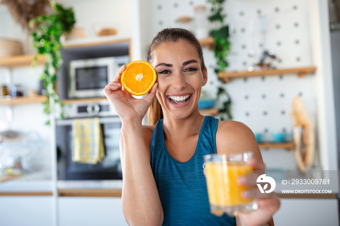 Beautiful young woman drinking fresh orange juice in kitchen. Healthy diet. Happy young woman with glass of juice and orange at table in kitchen.