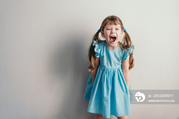 Screaming little girl in blue dress on neutral backgroung