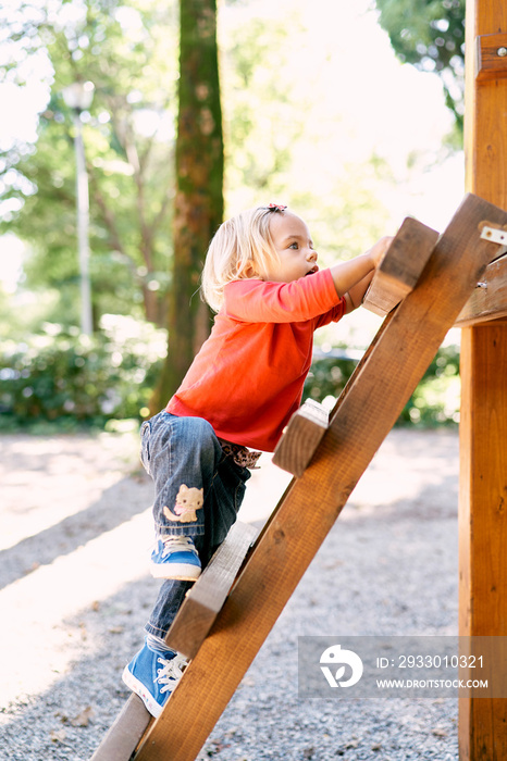 Little girl climbs the wooden stairs in the playground. High quality photo