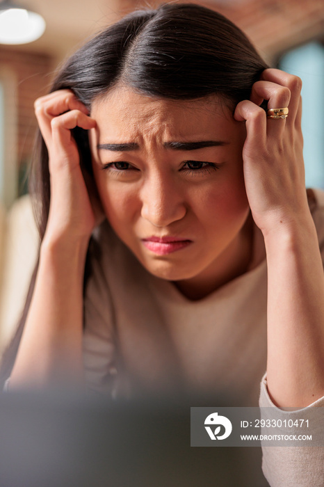 Young asian woman having migraine and headache while trying to work from home. Tired female on couch covering forehead and exhausted red eyes unhappy sick upset ill fever depresion