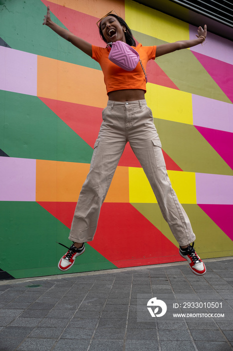 Smiling young woman jumping against colorful wall