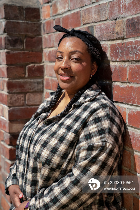 Portrait of woman wearing plaid shirt leaning against brick wall