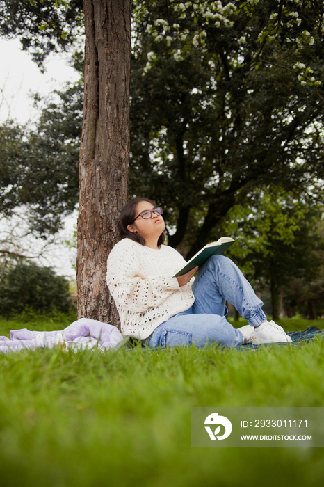 Curvy woman with Down syndrome reading and daydreaming in the park