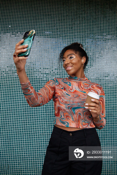 Curvy mixed-race woman with vitiligo taking a selfie in with coffee-to-go