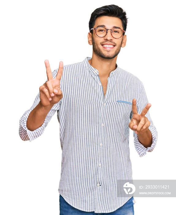 Young handsome man wearing casual clothes and glasses smiling looking to the camera showing fingers doing victory sign. number two.