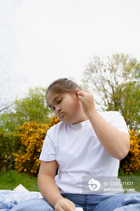 Young curvy woman with Down Syndrome sitting in a park with earbuds