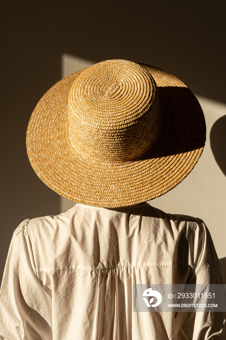 Young pretty woman in straw hat and white dress / sundress. Sunlight shadow on the wall. Minimal fashion design concept.