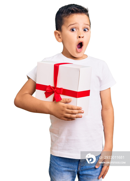 Little cute boy kid holding gift scared and amazed with open mouth for surprise, disbelief face