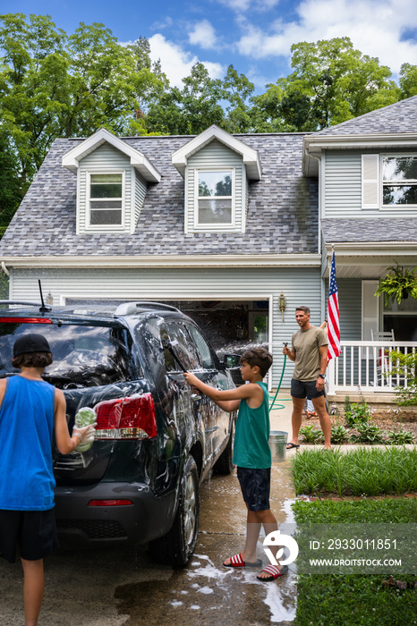 Air Force service member washes his vehicles with his sons in the driveway.