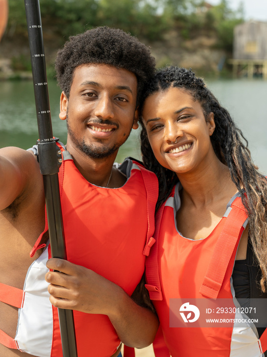 Portrait of smiling friends wearing life jackets and holding oar