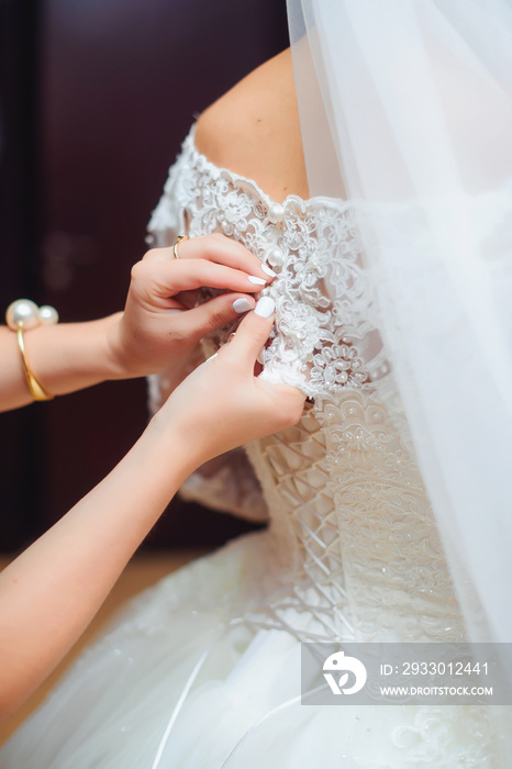 Wedding ceremony. Preparing the bride for the wedding.  White wedding dress. The corset on the dress. The texture of the fabric. Bride’s hands. White lace fabric.