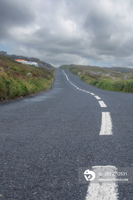 Road in focus, roof of a motor home in the background. Small highway in a country side. Travel concept. Low cloudy sky. Vertical image