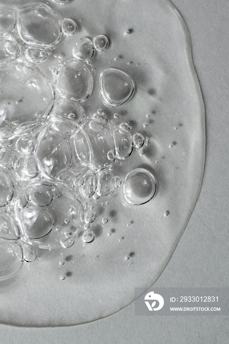 Transparent facial serum with bubbles on light grey background macro. Liquid bubbly gel with hyaluronic acid closeup. Moisturising cosmetic product texture. Beauty and spa concept. Top view.