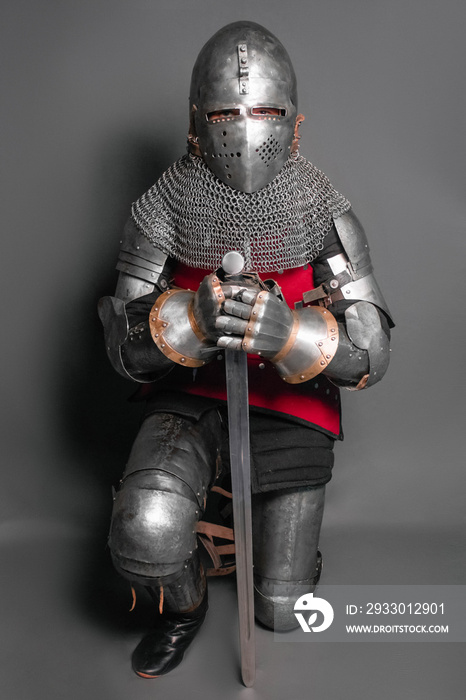 A young knight in medieval armor with a weapon in his hands kneeled.