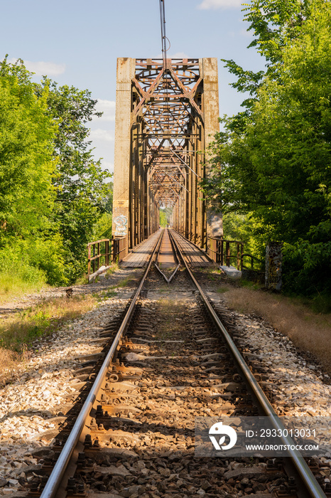 The metal structure of the railway viaduct over the river against the background of a blue sky with clouds.