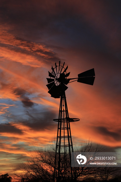 Kansas Sunset with a colorful sky with clouds and a farm Windmill silhouette that’s bright and colorful. That’s north of Hutchinson Kansas USA.