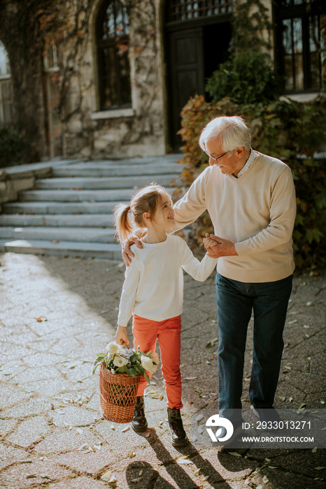 Grandfather having fun with his little granddaughter who holding basket full of flowers