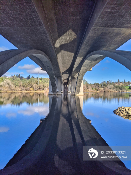 View under an concrete arched bridge with reflections on the water
