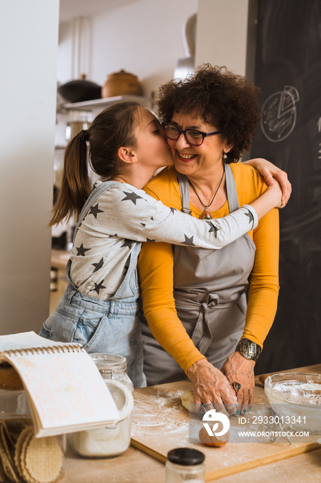 granddaughter kissing her grandmother while baking in kitchen