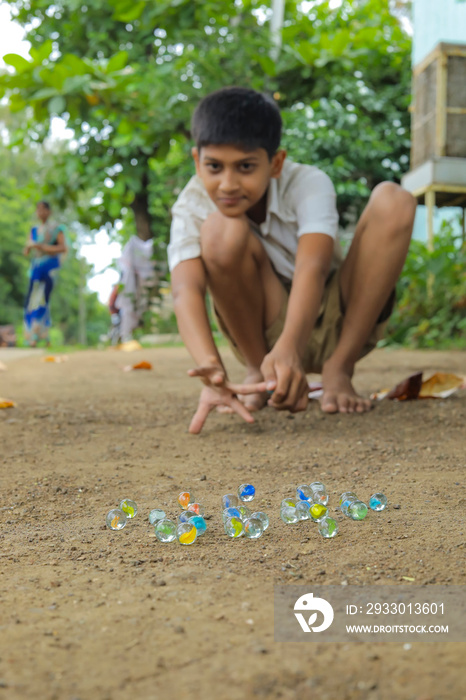 Indian child playing with glass marbles which is an old Indian village game. Glass Marbles are also called as Kancha in Hindi Language.