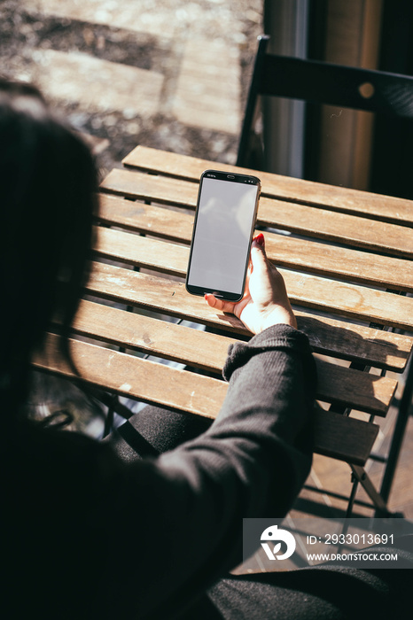 Smartphone similar to iphone 14 pro max with blank white screen for mockups, holding phone at home