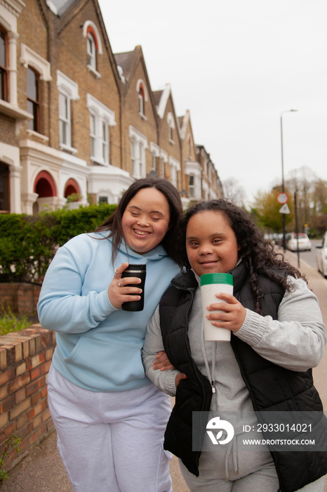 Two happy plus-sized women with Down Syndrome holding reusable coffee-to-go cups