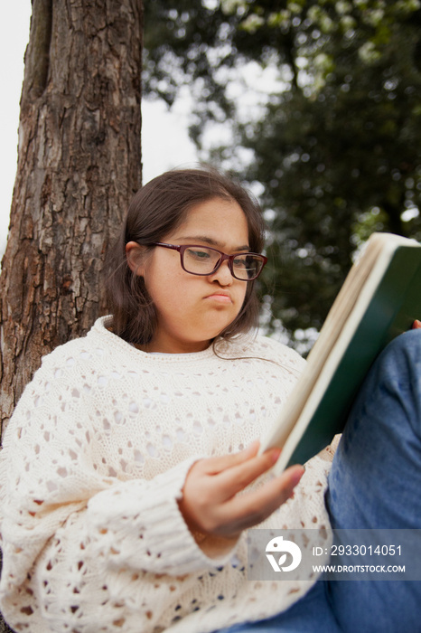 Curvy woman with Down syndrome reading in the park