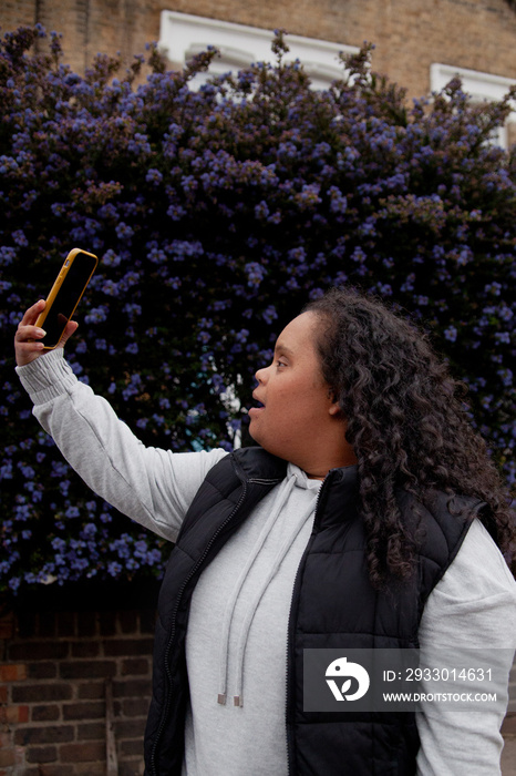 Young plus-sized women with Down Syndrome taking selfie in front of flowers