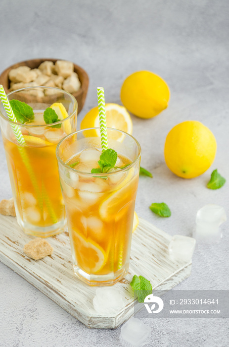 Ice tea with lemon, brown sugar, mint leaves and ice cubes in a glass on a board on a light background. Summer refreshing drink. Vertical orientation, copy space.