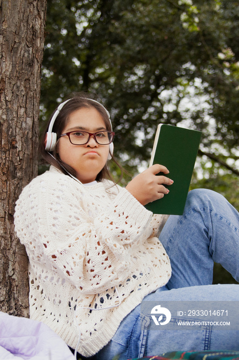 Happy woman with Down syndrome reading and listening to music in the park