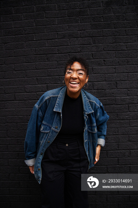 Mid-sized woman of mixed race in jeans jacket posing in front of black wall