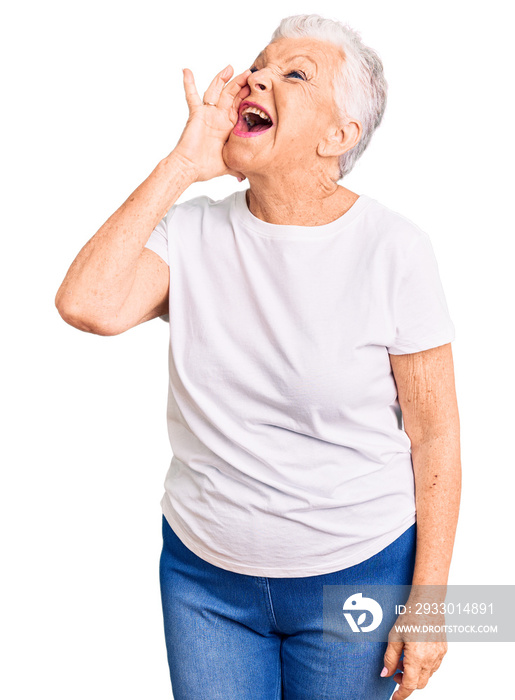 Senior beautiful woman with blue eyes and grey hair wearing casual white tshirt shouting and screaming loud to side with hand on mouth. communication concept.