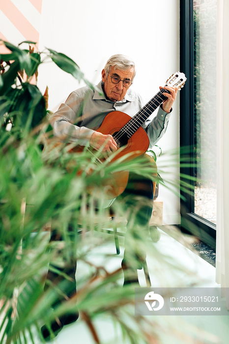 elderly man playing on acoustic guitar at home. senior person with music hobby.