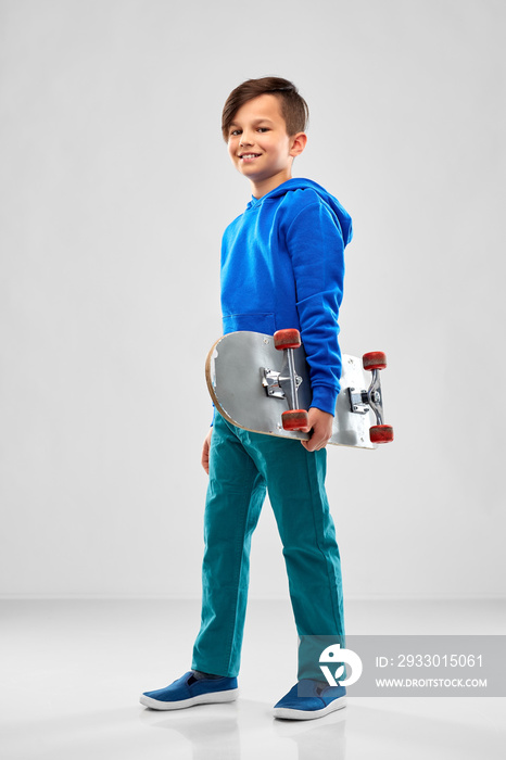 childhood, leisure and people concept - smiling boy in blue hoodie with skateboard over grey background