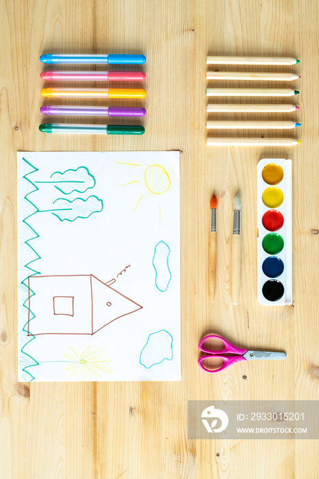 Child drawing on sheet of paper surrounded by supplies for drawing