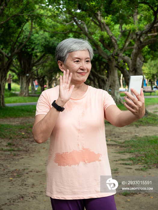 Portrait of senior adult elderly asian woman 60s smiling standing and holding smartphone in the park.