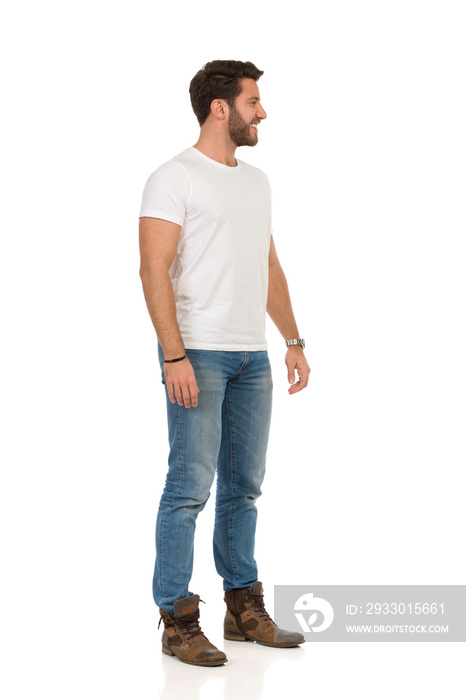 Handsome Man In Jeans And White T-shirt Is Standing, Smiling And Looking Away. Side View.