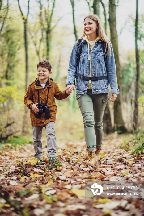 Happy mother and son are hiking in forest.