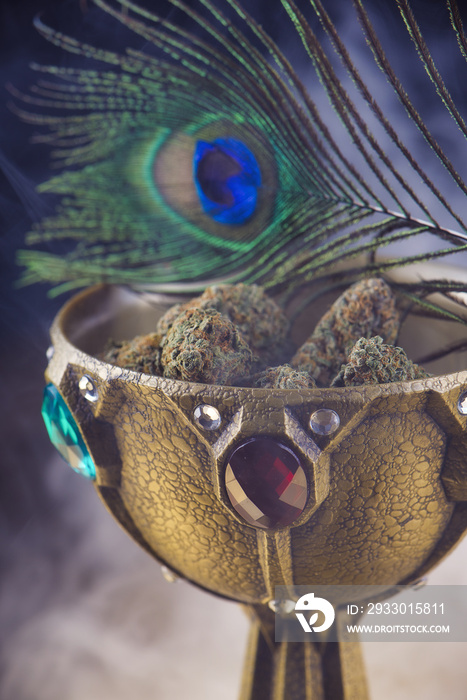 Close up detail of cannabis nugs on a calix with smoke and peacock feather