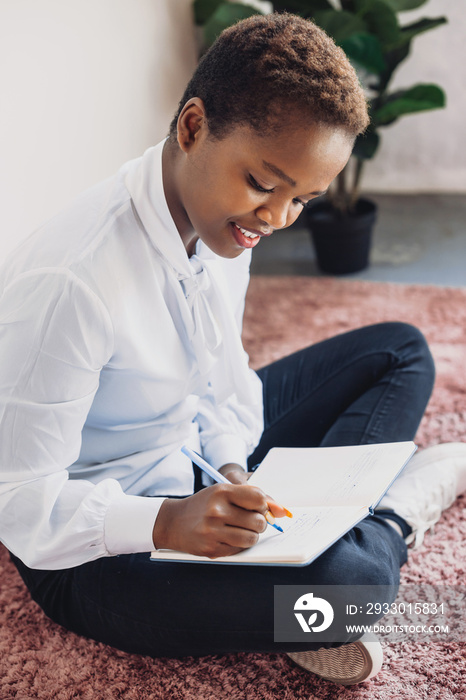 Pretty afro woman sitting on the floor and writing in notebook while studying alone at home. Modern business concept. People lifestyle concept. Underlines