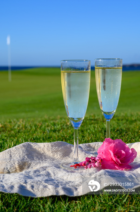 Two glasses with bubbles white champagne or cava wine served on green golf club grass with sea view for romantic event or celebration