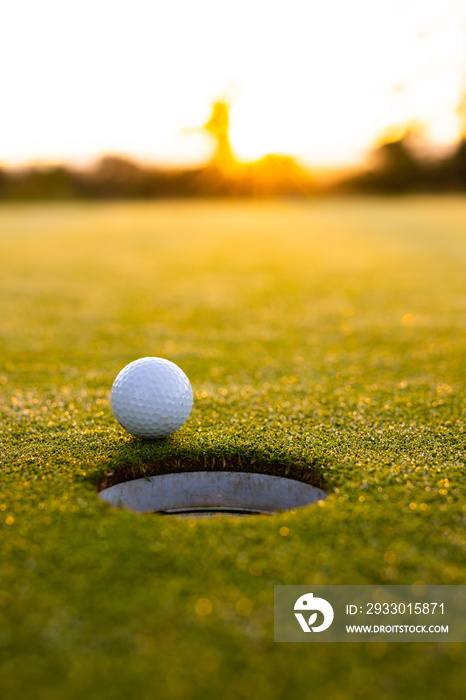 Close-up of white golf ball by hole on grassy land against clear sky at sunset, copy space