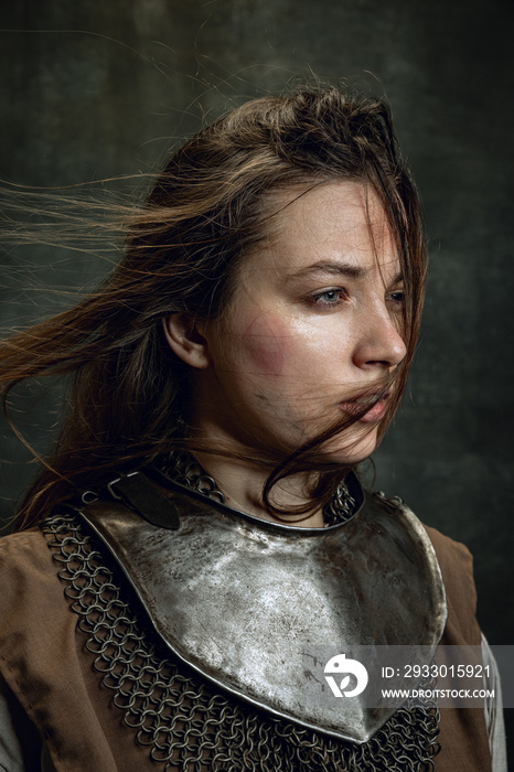 Close-up vintage portrait of adorable woman, medieval female warrior or knight with dirty wounded face looking away isolated over dark retro background.