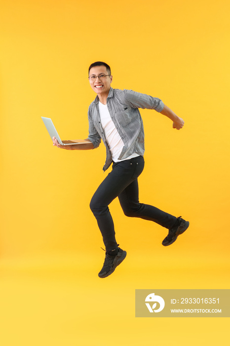 Happy jumping Asian programmer with laptop on color background