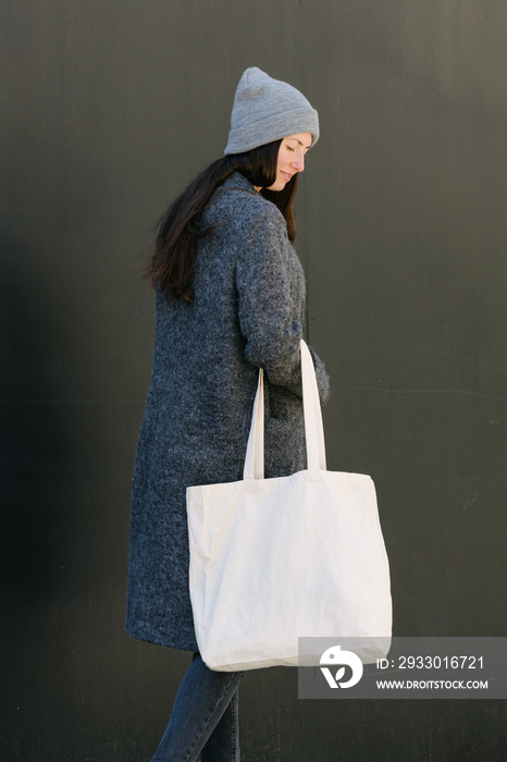 Woman holding white textile tote eco bag in urban area. Ecology or environment protection concept. White eco bag for mock up.