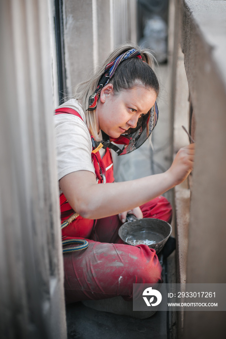 Woman worker standing on scaffolding and restore old building facade