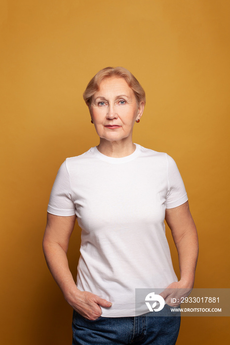 Mature woman in white t-shirt on bright yellow studio wall background